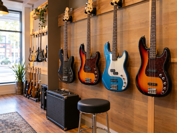 Electric bass guitars displayed on a wooden wall rack inside a warm, welcoming Tennessee guitar shop.